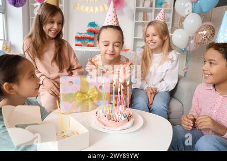 Süßes kleines Mädchen mit ihren Freunden, die sich auf der Geburtstagsfeier wünschen Stockfoto