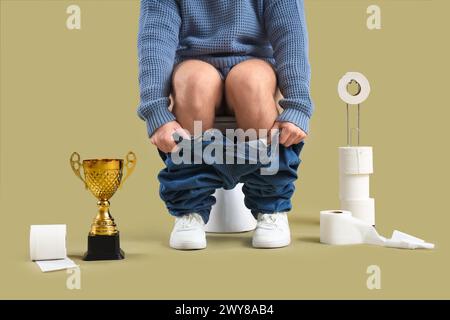 Junger Mann mit goldenem Becher, der auf einer Toilettenschüssel vor grünem Hintergrund sitzt Stockfoto