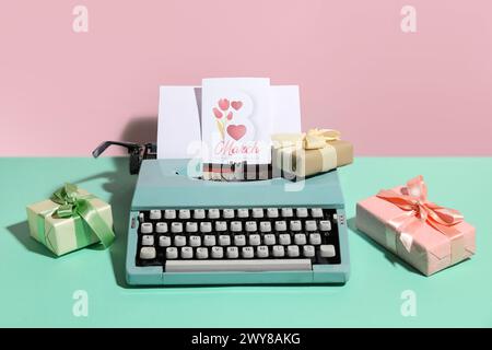 Vintage-Schreibmaschine, Geschenkboxen und Postkarte für den Frauentag auf türkisfarbenem Tisch vor rosa Hintergrund Stockfoto