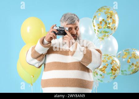 Senior Mann mit Ballons und Fotokamera auf blauem Hintergrund Stockfoto