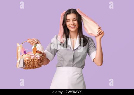 Glückliche Zimmermädchen in Hasenohren mit Osterkorb auf lila Hintergrund Stockfoto