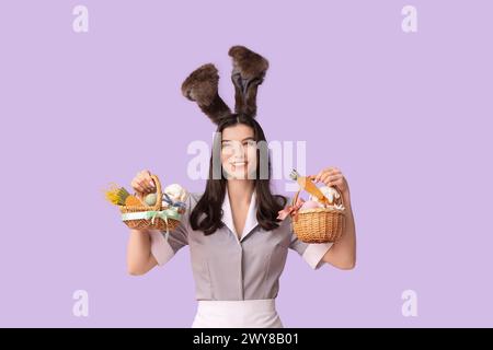 Glückliche Zimmermädchen in Hasenohren mit Osterkörben auf lila Hintergrund Stockfoto