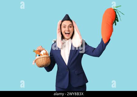 Glückliche Stewardess in Hasenohren mit Osterkorb und SpielzeugKarotte auf blauem Hintergrund Stockfoto