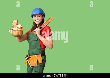 Glückliche Erbauerin mit Osterkorb, Wasserwaage und Werkzeugen auf grünem Hintergrund Stockfoto