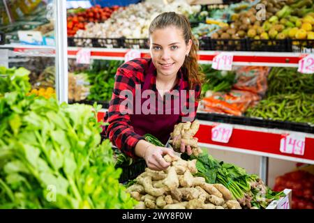 Lächelnde Verkäuferin legte Ingwer auf die Theke Stockfoto