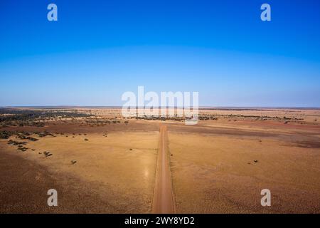 Aus der Vogelperspektive einer geraden Feldstraße, die durch eine trockene, trockene Landschaft unter einem klaren blauen Himmel führt Stockfoto