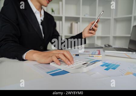 Buchhalterin verwendet Rechner, um den Gewinnprozentsatz des Unternehmens zu berechnen und Daten auf ihrem Handy zu betrachten Stockfoto