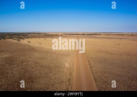 Gerade unbefestigte Straße, die durch eine karge Landschaft unter einem klaren blauen Himmel führt Stockfoto