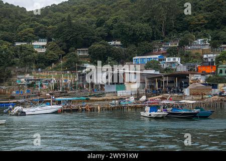 Traditionelle Bootswerft und Pfahlhäuser an der Küste eines Fischerdorfes in Hongkong. Kleine Boote legten an hölzernen Piers mit Häusern am Hügel und de an Stockfoto