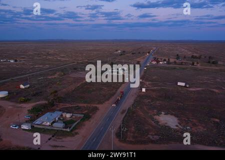 Aus der Vogelperspektive auf eine ruhige Straße, die in der Abenddämmerung durch eine ländliche Landschaft mit kargen Gebäuden führt Stockfoto