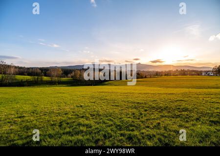 Der warme Glanz einer untergehenden Sonne taucht den Jested Mountain Ridge in Liberec und wirft lange Schatten über die grüne Wiese. Tschechien Stockfoto
