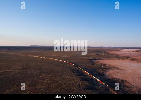 Aus der Vogelperspektive eines intermodalen Container-Güterzugs, der in der Abenddämmerung durch eine riesige Wüstenlandschaft in der Nähe von Port Augusta South Australia fährt Stockfoto