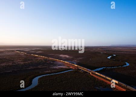 Aus der Vogelperspektive eines intermodalen Container-Güterzugs, der in der Abenddämmerung durch eine riesige Wüstenlandschaft in der Nähe von Port Augusta South Australia fährt Stockfoto