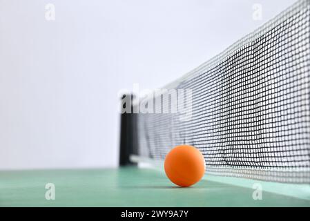 Pingpong-Hintergrund mit orangefarbener Kugel neben dem Netz auf einem grünen Spieltisch und weißem isolierten Hintergrund. Vorderansicht. Stockfoto