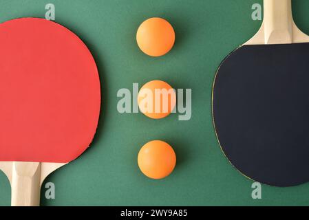 Komposition mit Tischtennispaddles und drei orangen Kugeln auf grünem Spieltisch. Draufsicht. Stockfoto