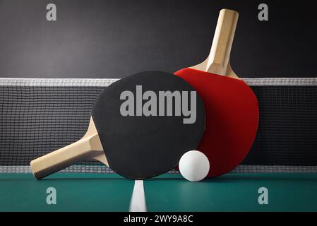 Blick auf das professionelle Tischtennisset mit Paddles, die auf dem Netz auf dem grünen Spieltisch mit weißem Ball liegen. Vorderansicht. Stockfoto