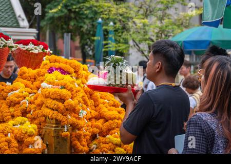 Im Herzen der Innenstadt von Bangkok, am Erawan-Schrein, bietet ein asiatischer Mann seine Gebete an und überreicht einen Korb mit Früchten, die als Opfergabe gekauft wurden. Bangkok, Thailand. Stockfoto