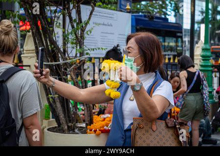 Im Erawan-Schrein in der Innenstadt von Bangkok macht eine ältere asiatische Frau ein Selfie mit ihrer Blumengirlande, die für ein Opferangebot gekauft wurde. Bangkok, Thailand. Stockfoto