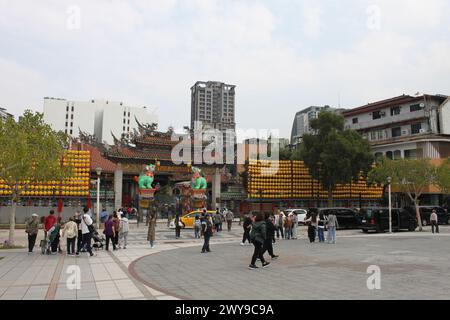 Taipei City, Taiwan - 17. März 2024: Eingangstür zum Longshan Tempel, Taipeh. Geschäftige Straße, Besucher, Einheimische, Laternen, Wolkenkratzer. Moderne Zeiten treffen Stockfoto