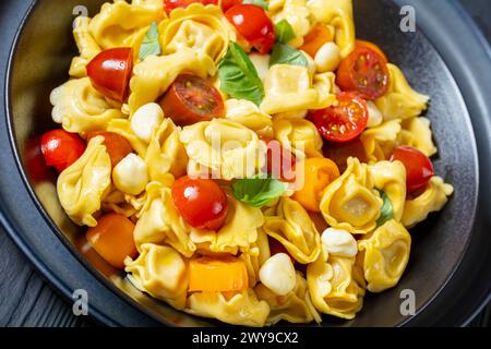 Nahaufnahme von Tortellini-Salat mit Kirschtomaten, Mini-Mozzarella, frischen Basilikumblättern in schwarzer Schüssel Stockfoto