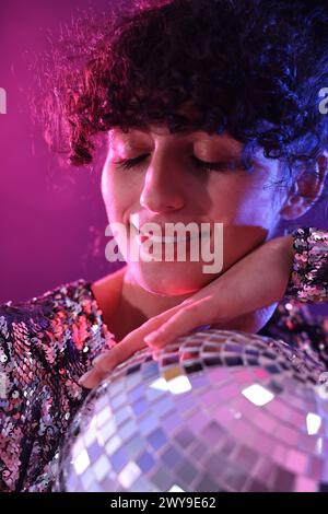 Schöne junge Frau mit Discoball, die auf farbigem Hintergrund in Neonlichtern posiert, Nahaufnahme Stockfoto