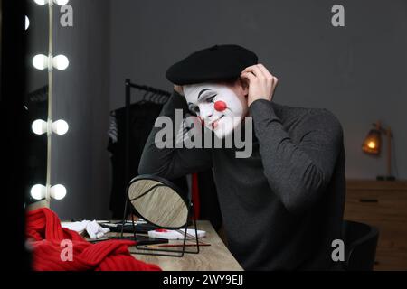 MIME-Künstler, der Baskenmütze in der Nähe des Spiegels in der Garderobe auflegt Stockfoto
