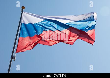 Die Nationalflagge Russlands, auch bekannt als Staatsflagge der Russischen Föderation, steht an einem sonnigen Tag unter hellblauem Himmel Stockfoto