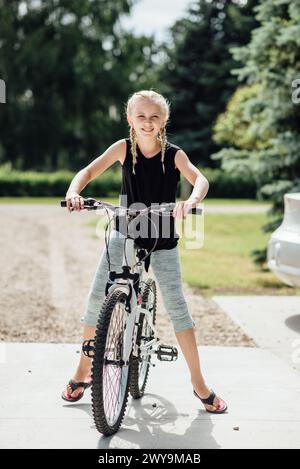 Vorderansicht eines jungen Mädchens, das auf dem Fahrrad steht und im Hof lächelt Stockfoto