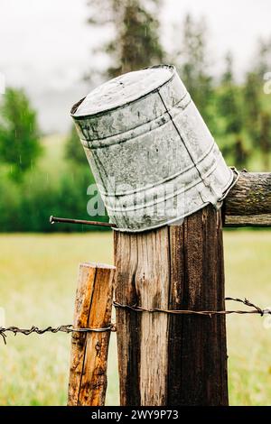 Auf dem Kopf hängende Blechkübel auf dem Holzzaun an regnerischen Tagen Stockfoto