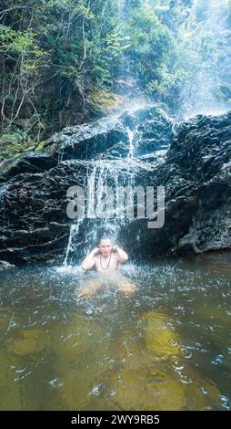 Ein Mann in Glückseligkeit unter dem Rauschen eines üppigen Wasserfalls. Stockfoto