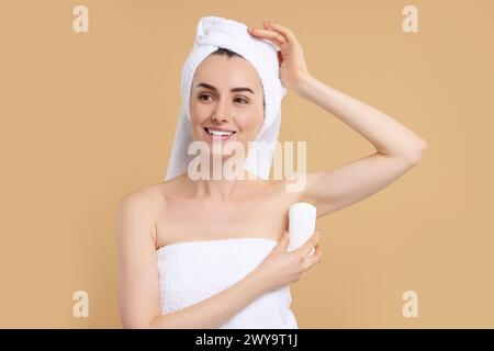 Schöne Frau, die Deodorant auf beigefarbenem Hintergrund aufträgt Stockfoto