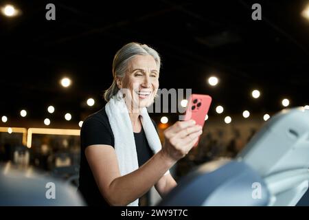 Lustige, hübsche Seniorsportlerin mit grauem Haar, die beim Training auf dem Laufband im Fitnessstudio Videoanruf hat Stockfoto