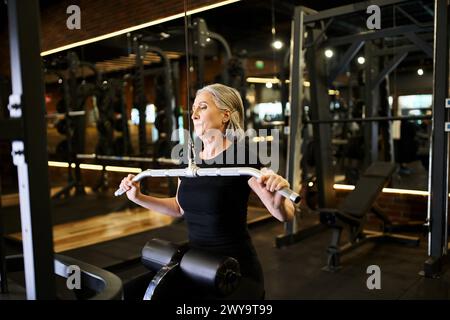 Ziemlich athletische Seniorin in Sportbekleidung mit Handtuch, die auf Lats Pulldown-Maschine im Fitnessstudio trainieren Stockfoto