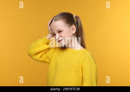 Kleines Mädchen mit Kopfschmerzen auf gelbem Hintergrund Stockfoto