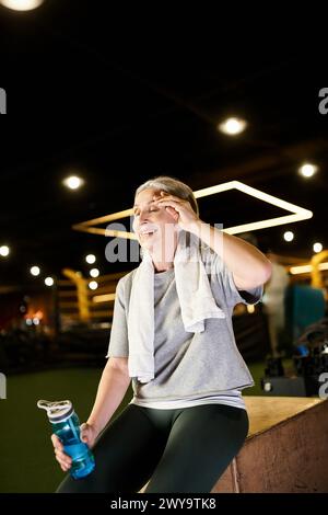 Reife, fröhliche, hübsche Frau in Sportbekleidung mit Handtuch und Wasserflasche, die sich nach dem Training entspannt Stockfoto