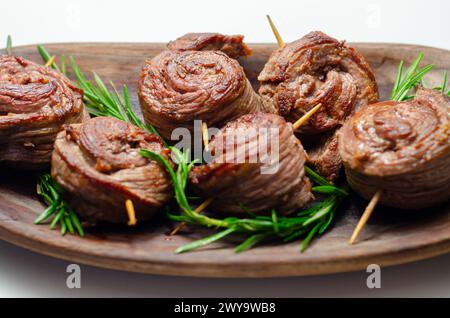 Ein Teller mit Fleischstücken in Form von Rosen mit grünen Kräutern darauf. Die Rindfleischstücke sind klein und rund, und sie sitzen auf einer Holzplatte Stockfoto