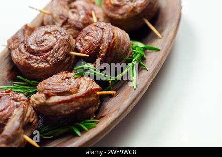 Ein Teller mit Fleischstücken in Form von Rosen mit grünen Kräutern darauf. Die Rindfleischstücke sind klein und rund, und sie sitzen auf einer Holzplatte Stockfoto