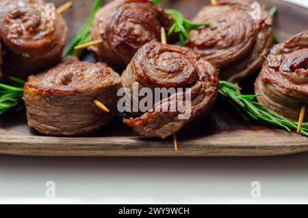 Ein Teller mit Fleischstücken in Form von Rosen mit grünen Kräutern darauf. Die Rindfleischstücke sind klein und rund, und sie sitzen auf einer Holzplatte Stockfoto