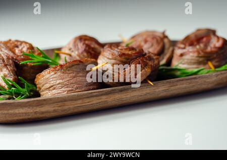 Ein Teller mit Fleischstücken in Form von Rosen mit grünen Kräutern darauf. Die Rindfleischstücke sind klein und rund, und sie sitzen auf einer Holzplatte Stockfoto