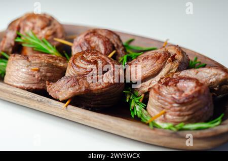 Ein Teller mit Fleischstücken in Form von Rosen mit grünen Kräutern darauf. Die Rindfleischstücke sind klein und rund, und sie sitzen auf einer Holzplatte Stockfoto