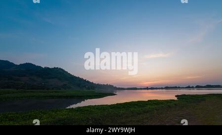 Sanfte Pastelltöne des Sonnenuntergangs über einem ruhigen See mit sanften Hügeln und einer klaren Reflexion auf dem Wasser. Stockfoto