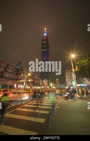 Die belebte Straßenszene mit bewegtem Verkehr und Fußgängern führt zum beleuchteten Turm Taipei 101 vor dem dunklen Himmel nach dem Silvesterfeuerwerk Stockfoto