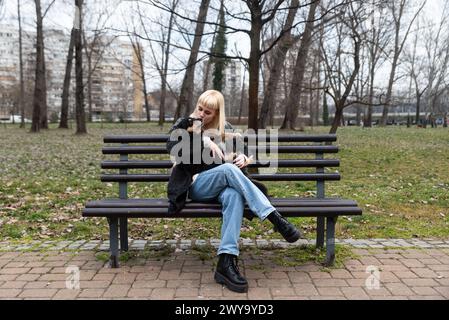 Junge Generation Z Hipster Mädchen sitzt auf einer Bank im Park mit ihrem adoptierten Hund, den sie von der Straße vor dem Hunger gerettet hat und ihm Liebe schenkt Stockfoto