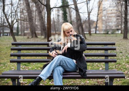 Junge Generation Z Hipster Mädchen sitzt auf einer Bank im Park mit ihrem adoptierten Hund, den sie von der Straße vor dem Hunger gerettet hat und ihm Liebe schenkt Stockfoto