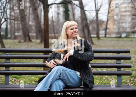 Junge Generation Z Hipster Mädchen sitzt auf einer Bank im Park mit ihrem adoptierten Hund, den sie von der Straße vor dem Hunger gerettet hat und ihm Liebe schenkt Stockfoto