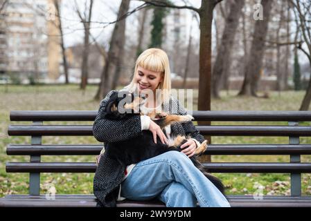 Junge Generation Z Hipster Mädchen sitzt auf einer Bank im Park mit ihrem adoptierten Hund, den sie von der Straße vor dem Hunger gerettet hat und ihm Liebe schenkt Stockfoto