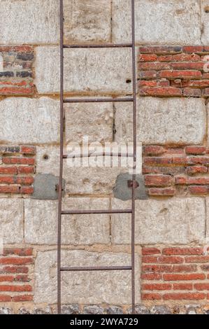 Ein senkrechter Schuss einer rostigen alten Leiter gegen eine Steinmauer Stockfoto