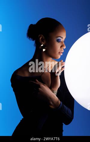 Eine junge afroamerikanische Frau hält anmutig einen großen weißen Ball in den Händen in einem Studio-Setting. Stockfoto