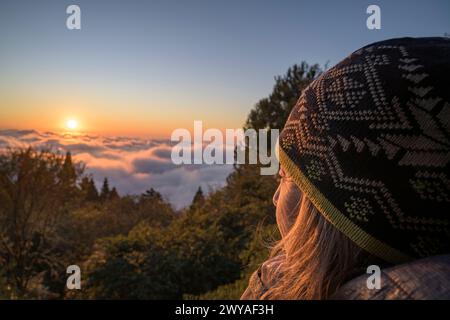 Nahaufnahme einer Frau in warmer Kleidung, die einen ruhigen Sonnenuntergang über einem Wolkenmeer von einem hohen Aussichtspunkt im Alishan National Park genießt Stockfoto