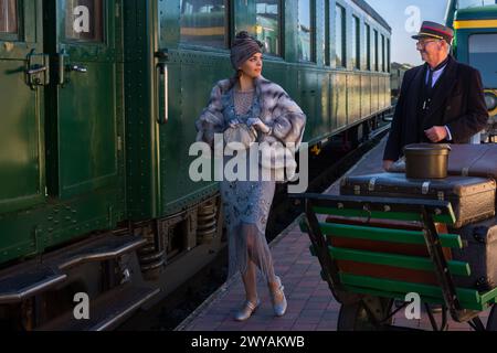 Nachstellungsszene auf dem Bahnsteig in der Nähe eines authentischen 1927 First Class Zugwaggons, wo eine schicke 1920er Dame auf ihr Gepäck wartet Stockfoto